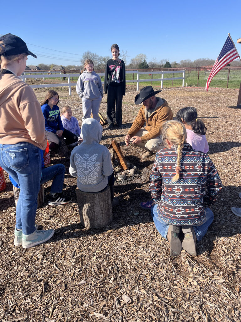 Camp staff member teaching campers how to build a fire outdoors at Hidden Pastures Fall Break Farm Camp