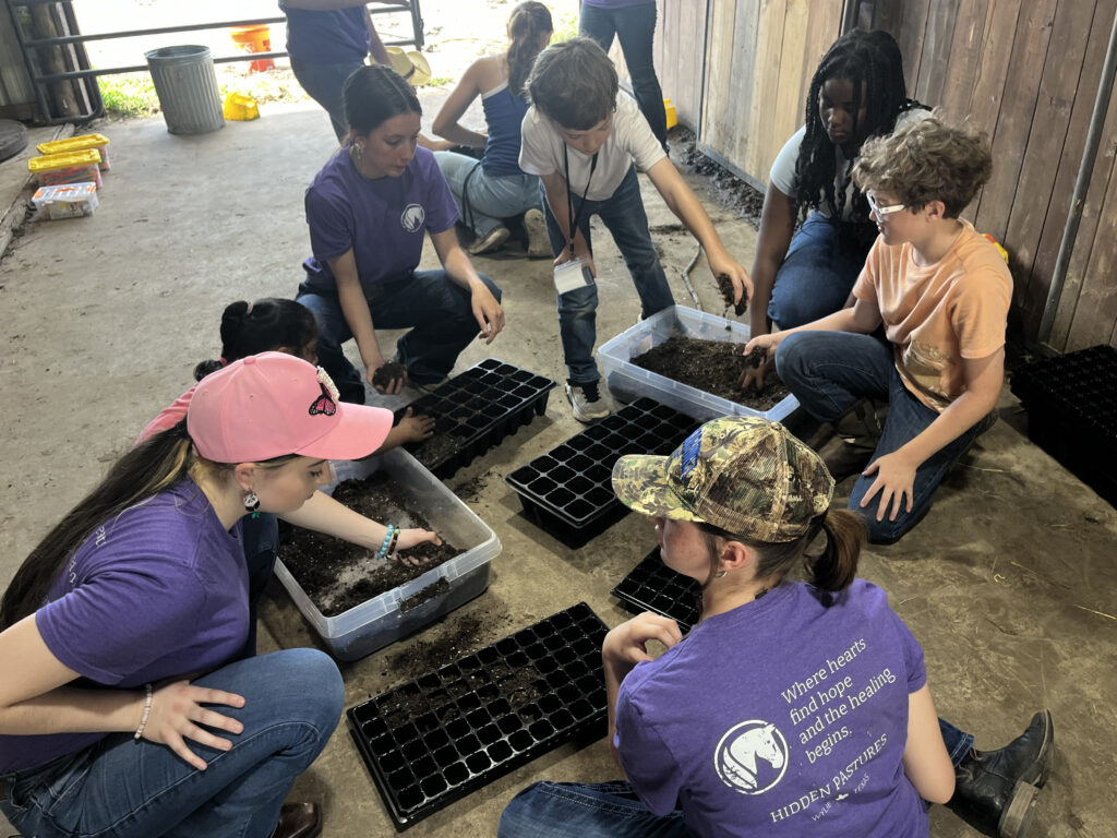 Campers planting seedlings together in trays at Hidden Pastures Spring Break Farm Camp