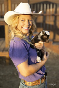 A woman in a cowboy hat holding a baby goat at Hidden Pastures