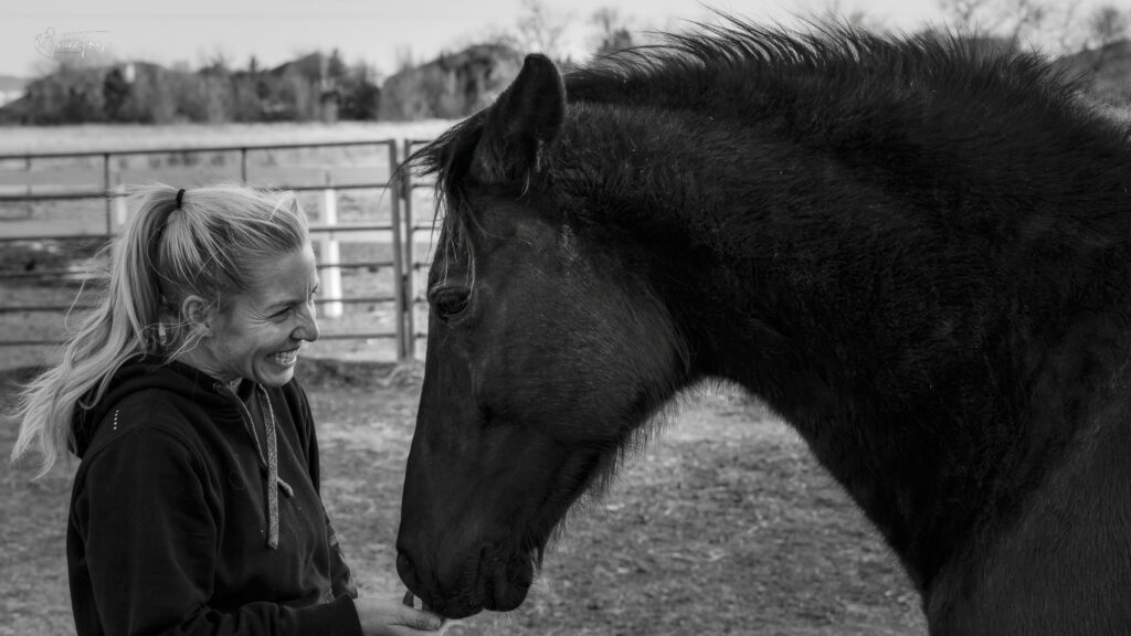 A woman smiling with a horse in a black and white photo at Hidden Pastures Women at the Farm